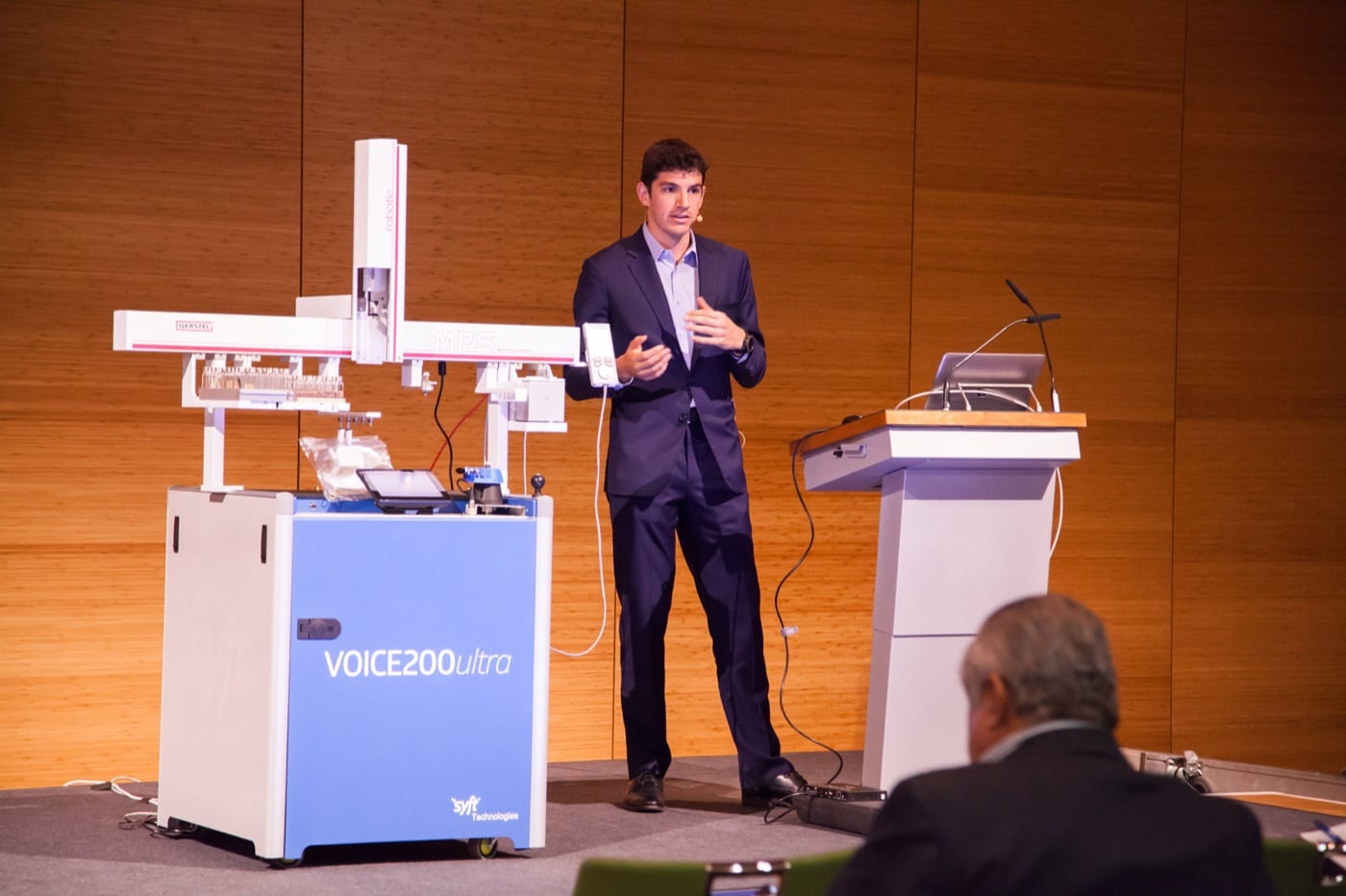 David presenting on stage beside a Syft VOICE 200ultra mass spectrometer.